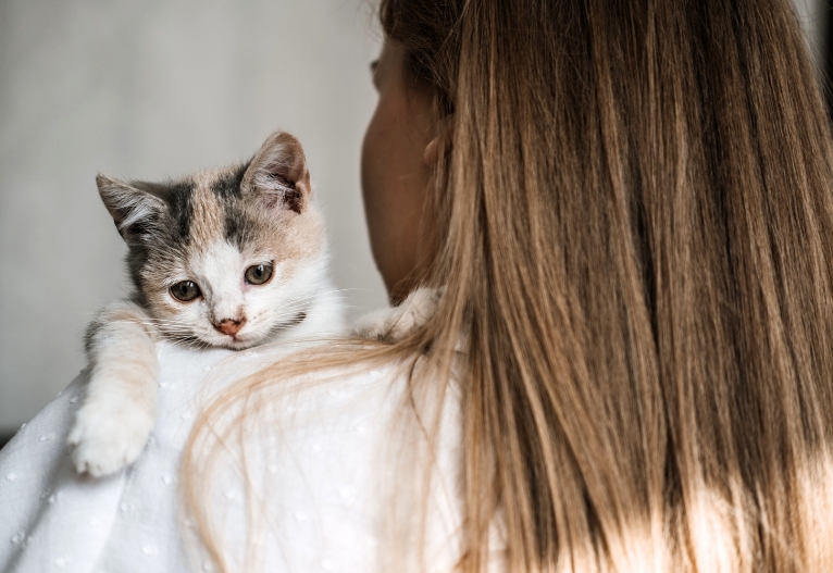 Woman holding a kitten over her shoulder.