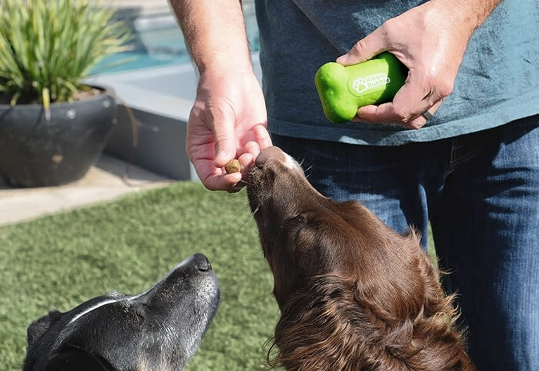 Person giving dogs a treat from a green silicone pouch.