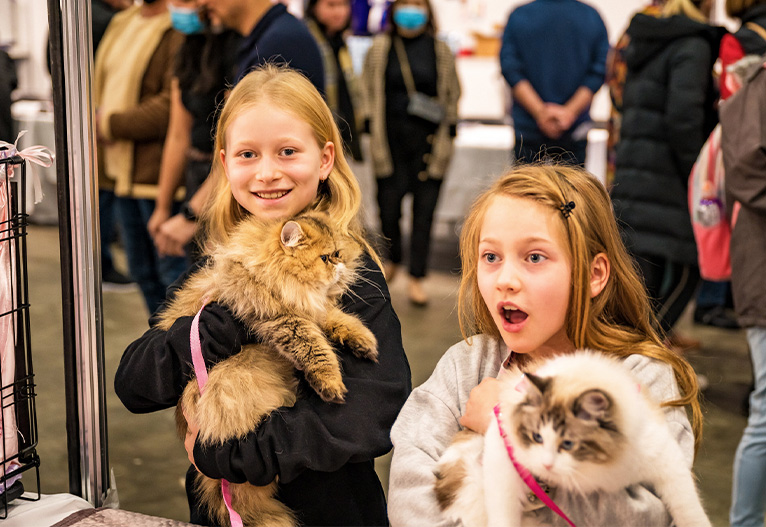 Two young girls holding cats at the Cat Lovers Festival.