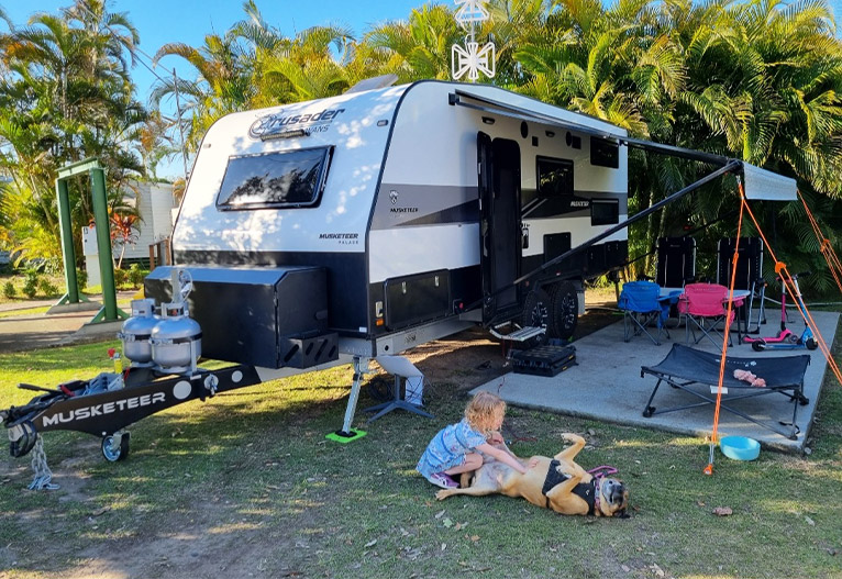 Child tickling her dog outside a caravan.
