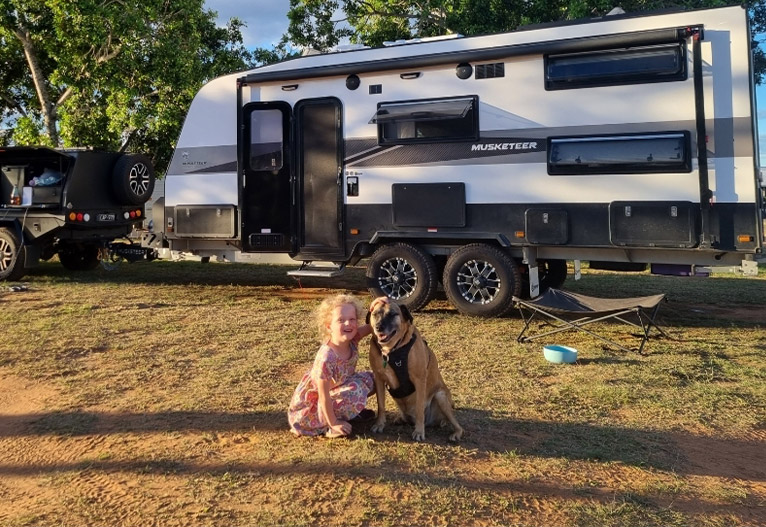 Child and dog outside a caravan.