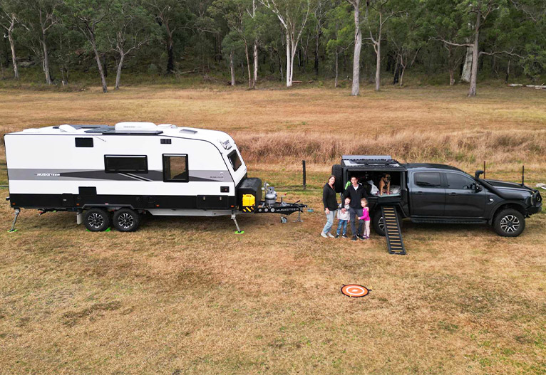 Family with a dog in front of their car and caravan.
